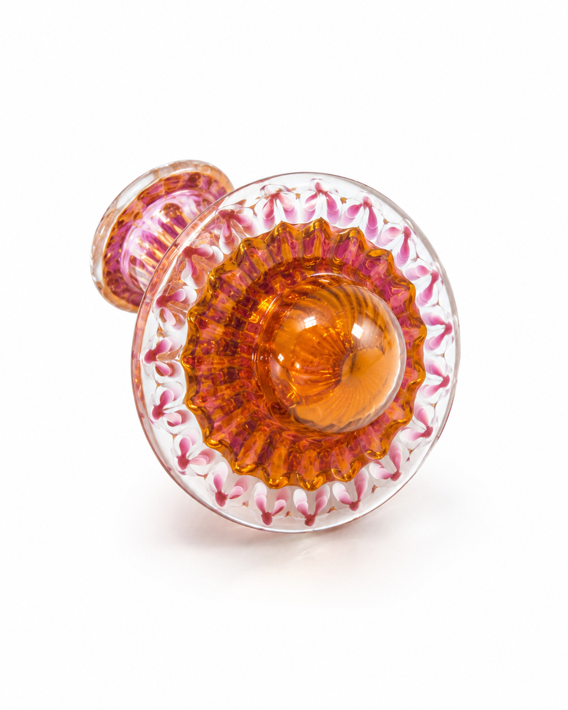 A decorative glass cabochon knob with a translucent amber-orange center, surrounded by a scalloped pink and white patterned border, on a white background.